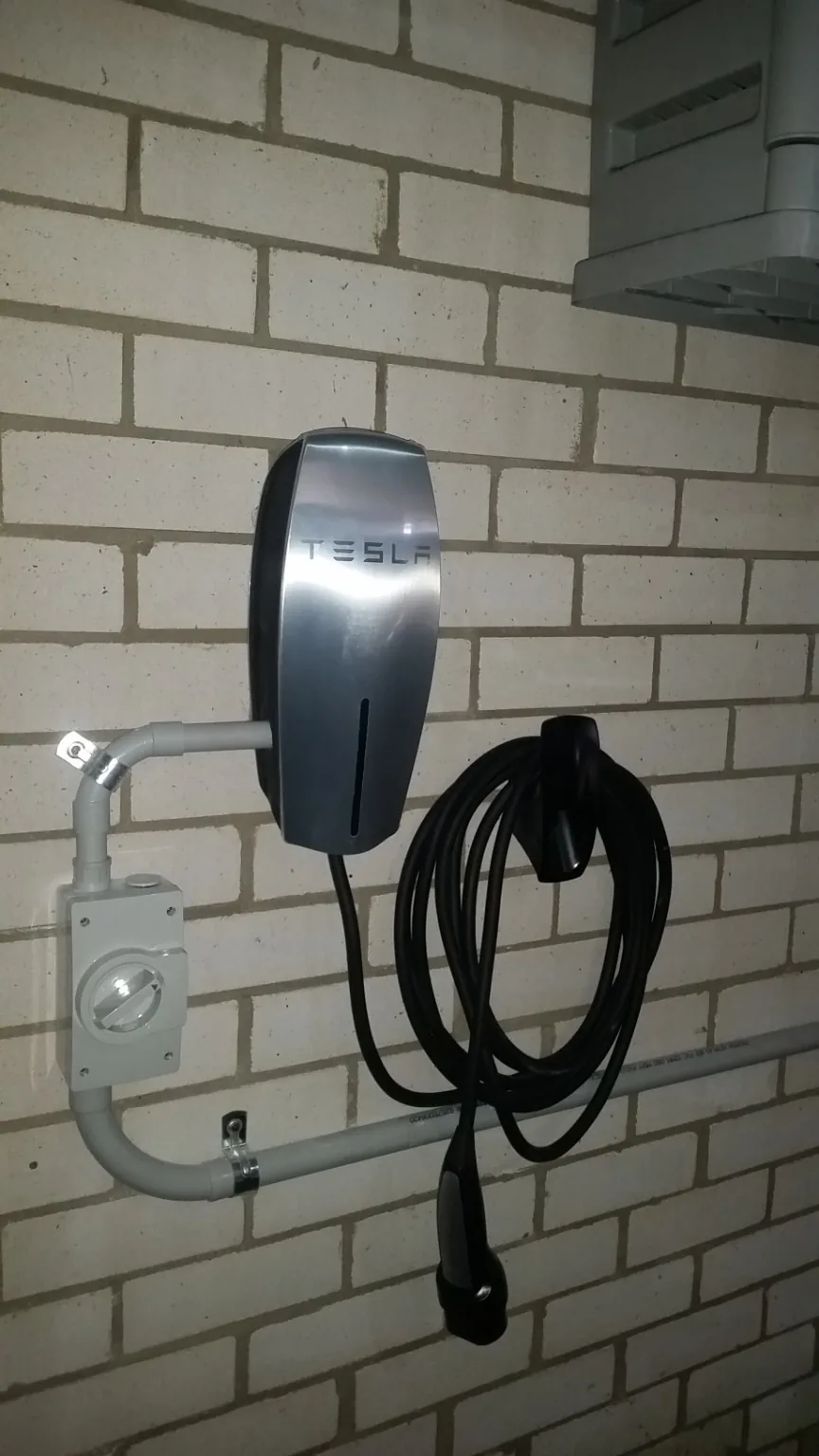 Tesla Wall Connector installed on brick garage wall with charging cable