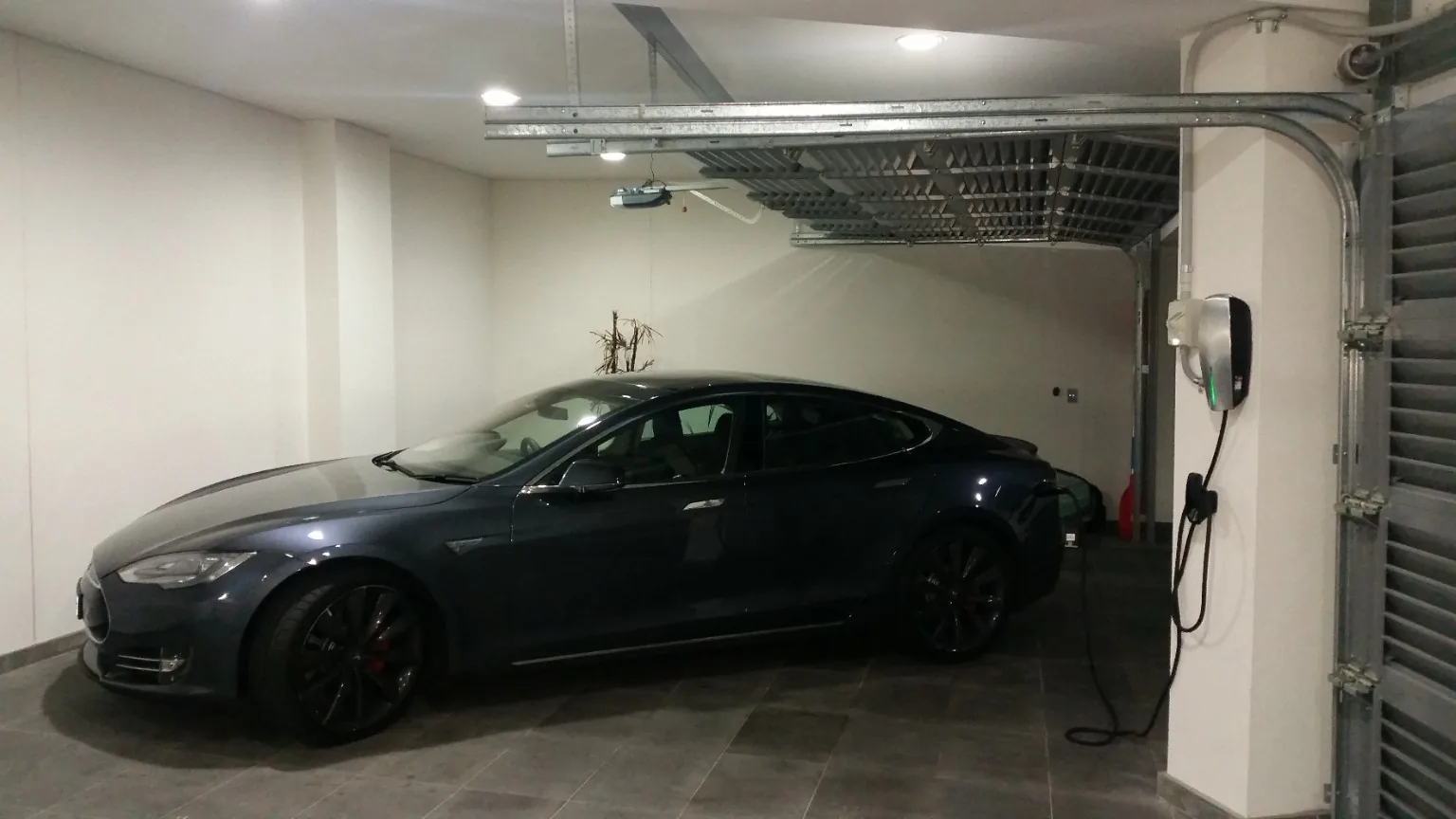 Tesla electric vehicle parked in garage beside installed Tesla Wall Connector